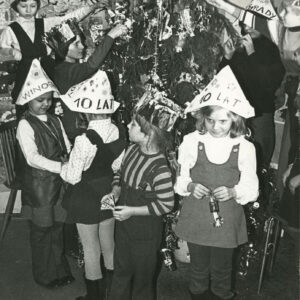 grupa dzieci ubierających choinkę, część z nich nosi papierowe czapki