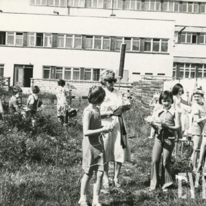 grupa dzieci z opiekunką malujących po płocie, w tle budynek z cegieł