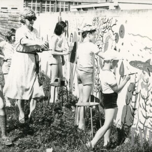 grupa dzieci z opiekunką malujących po płocie