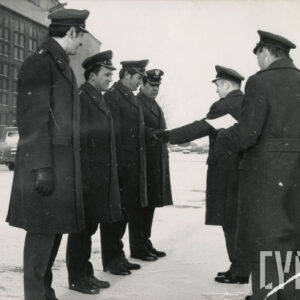 siedmiu mężczyzn w wojskowych płaszczach i czapkach na płycie lotniska, pora zimowa