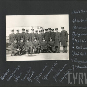 kilkunastu mężczyzn w mundurach, płaszczach wojskowych i czapkach upozowani w dwóch rzędach, pierwszy rząd w przyklęku, na tle fragmentu samolotu wojskowego 