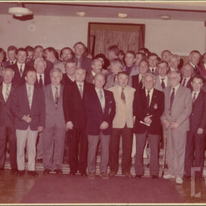 kilkudziesięciu mężczyzn w garniturach, część z nich w mundurach wojskowych, stoją w kilku rzędach, pozując do zdjęcia, zdjęcie wykonane w pomieszczeniu