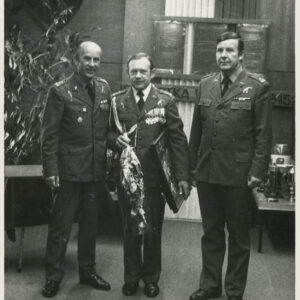 trzech mężczyzn w mundurach, mężczyzna w środku trzyma kwiaty