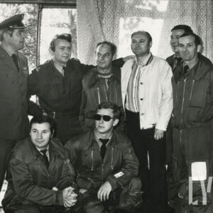 kilku mężczyzn w pomieszczeniu, kilku z nich w mundurach wojskowych i kombinezonach lotniczych