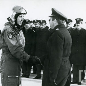 duża grupa mężczyzn w mundurach wojskowych stoi na baczność, na pierwszym planie mężczyzna w kombinezonie lotniczym podaje rękę mężczyźnie w mundurze wojskowym