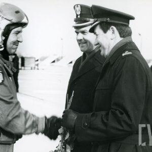 z lewej mężczyzna w kombinezonie pilota wojskowego i hełmie wita się z dwoma mężczyznami w mundurach wojskowych i czapkach, za nimi, w głębi mężczyzna w kurtce i berecie wojskowym z orzełkiem