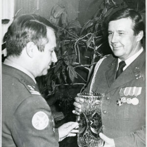 dwóch mężczyzn w mundurach wojskowych, jeden podaje drugiemu kryształowy wazon