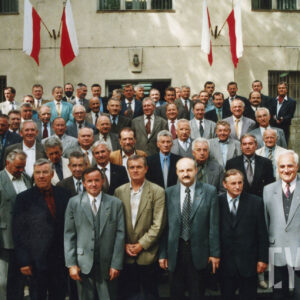 duża grupa mężczyzn w garniturach pozuje na schodach przed murowanym budynkiem do zdjęcia, na budynku flagi państwowe biało-czerwone