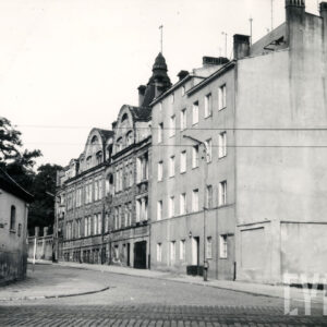 kilkukondygnacyjne kamienice, na pierwszym planie prosty budynek, za nim kamienice z ozdobnym szczytem