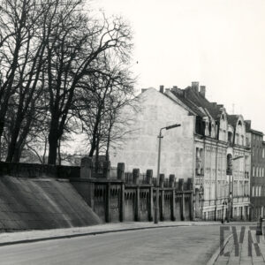 asfaltowa ulica, z lewej skarpa z ozdobnym murem, w głębi kilkukondygnacyjne kamienice