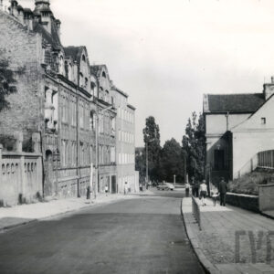 asfaltowa ulica, z lewej kilkukondygnacyjne kamienice, z prawej niski budynek