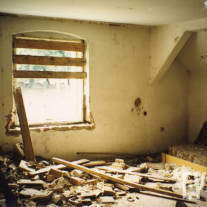 pomieszczenie z oknem, częściowo przysłoniętym deskami, na podłodze porozrzucany gruz i cegły