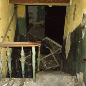 widok z góry schodów na zniszczone wnętrze, z łuszczącą się i odpadającą farbą, na podłodze gruz i fragmenty ram okiennych