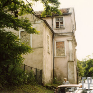 budynek przy ulicy z zamurowanymi oknami, z lewej fragment drzewa, w głębi drzewa