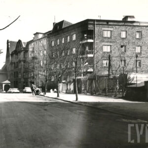 asfaltowa ulica, przy niej kilkukondygnacyjne budynki mieszkalne