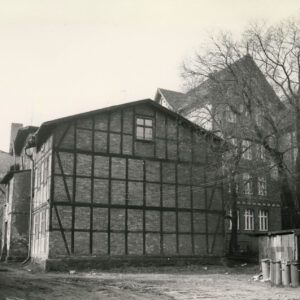 budynek mieszkalny drewniano-ceglany, z prawej niskie drewniane szopki