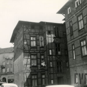 czterokondygnacyjny, drewniano-ceglany budynek, w głębi z lewej fragment kilkukondygnacyjnej kamienicy