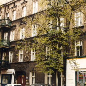 czterokondygnacyjna kamienica z bogatą dekoracją rzeźbiarską, przed nią wysokie drzewa