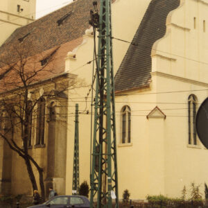 fragment budynku kościoła, na pierwszym planie kratownicowy słup metalowy sieci trakcji tramwajowej