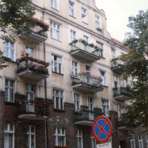 trzypiętrowa kamienica z przyziemiem i częścią mieszkalną w szczycie budynku, przed kamienicą drzewa i zaparkowane samochody