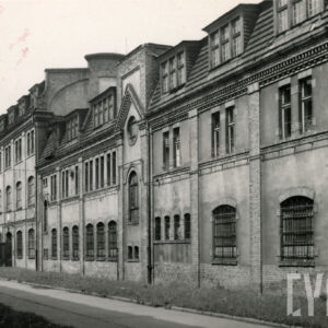 wzdłuż drogi dwa budynki z dosyć bogatą dekoracją na elewacji, z prawej budynek trzykondygnacyjny z mansardowymi oknami w dachu, z lewej czterokondygnacyjny z mansardowymi oknami w dachu