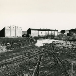 na pierwszym planie gruntowa droga, w głębi dwa budynki gospodarcze