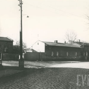 brukowana ulica, przy niej jednokondygnacyjne, ceglane i otynkowane budynki domy mieszkalne, z lewej dochodzi ulica gruntowa, na skrzyżowaniu słup energetyczny