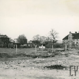 na pierwszym planie użytek rolny, w głębi z prawej ceglany, dwukondygnacyjny dom mieszkalny, z lewej niska zabudowa mieszkalna i gospodarcza