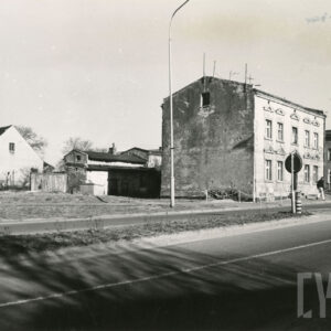 na pierwszym planie asfaltowa ulica, z prawej jednopiętrowy ceglany dom mieszkalny, z lewej w głębi murowany dom mieszkalny ze spadzistym dachem