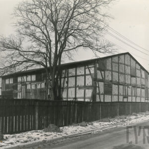 stodoła o konstrukcji szachulcowej stojąca szczytem do ulicy, przed nią drewniany płot, za płotem pozbawione liści drzewo