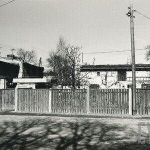 na pierwszym planie ulica, dalej drewniany plot, za nim zabudowania gospodarcze