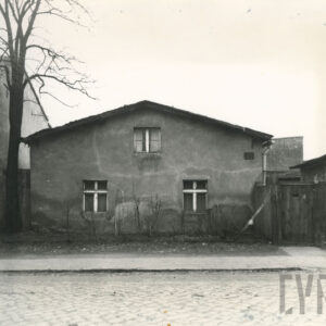 szczytowa ściana murowanego domu za drucianym płotem, po prawej płot drewniany, po lewej duże drzewo