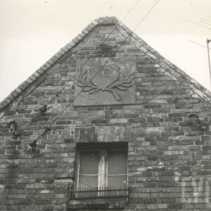 ceglany szczyt budynku z oknem i ozdobnym elementem roślinnym nad nim