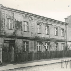 murowany dom ze zniszczoną elewacją i odpadającym tynkiem, piętrowy, z rzędami okien na parterze i piętrze, przed domem drewniany płot