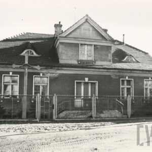 elewacja frontowa parterowego domu z poddaszem krytego spadzistym dachem z wykuszem i lukarnami, przed nim krzyż i druciany płot