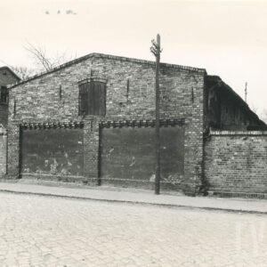 ściana szczytowa ceglanej stodoły ze spadzistym dachem, po prawej ceglane ogrodzenie posesji