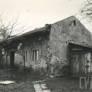 dom mieszkalny ze spadzistym dachem z odpadającym tynkiem i drewutnią przystawioną do ściany szczytowej