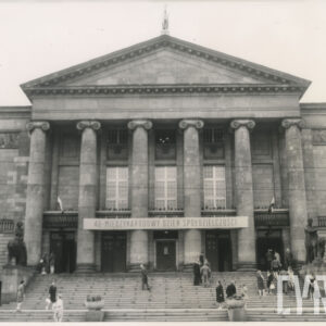 gmach z trójkątnym szczytem i kolumnami, nad wejściem napis, na schodach do budynku grupki ludzi