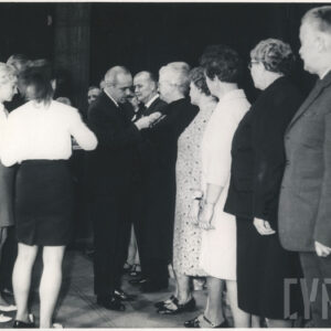 w jednym rzędzie stoją mężczyźni i kobiety, mężczyzna dekoruje jedną z osób, przy nim stoją dwie młode kobiety