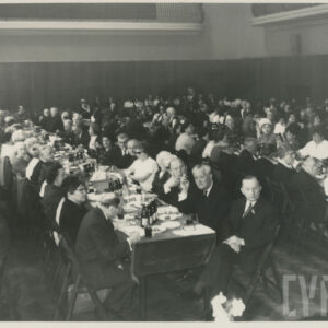 ludzie siedzą przy długich stołach, ustawionych równolegle do siebie