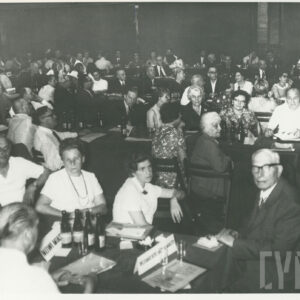 ludzie siedzą przy długich stołach, ustawionych równolegle do siebie, na stołach butelki, szklanki, notatki