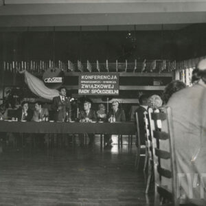 dwa stoły ustawione w kształcie litery L , przy nich siedzą ludzie