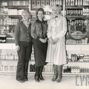 trzy kobiety stoją przed ladą sklepową i pozują do zdjęcia, za nimi półki z artykułami kosmetycznymi