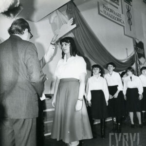 młode kobiety w jasnych bluzkach i ciemnych spódnicach podchodzą po kolei do mężczyzny zwróconego do nich przodem