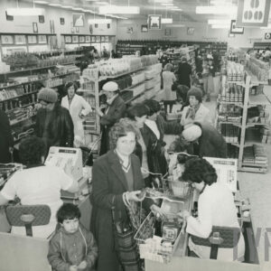 półki z artykułami w dużym sklepie, między półkami klienci, na pierwszym planie dwie kasy przy których siedzą dwie kobiety, przy kasach kolejka klientów