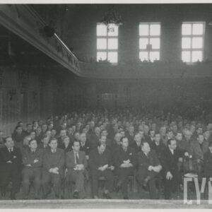 wnętrze dużej sali, na krzesłach ustawionych prostopadle w rzędach siedzą mężczyźni