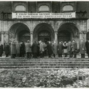 wejście do budynku ozdobione trzema arkadami, nad wejściem napis, przed wejściem duża grupa ludzi