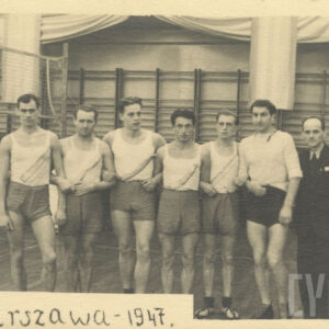 sześciu mężczyzn w strojach sportowych i krótkich spodenkach w sali sportowej, obok nich , z prawej mężczyzna w ciemnym garniturze