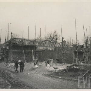 plac budowy, ceglana ściana, przy niej drewniane rusztowania, na placu pracują mężczyźni