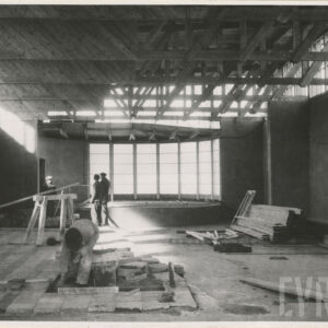 wnętrze budowanego pawilonu, murowane ściany, w głębi duże okno, drewniana konstrukcja dachu, pracujący robotnicy